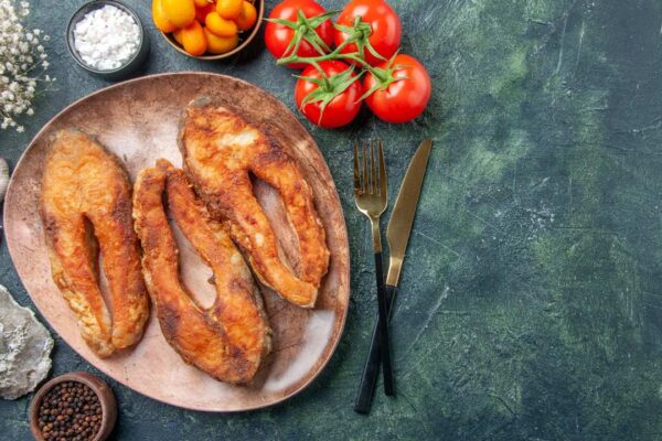 Peixe frito em prato, acompanhado de tomate, alho e outros ingredientes.
