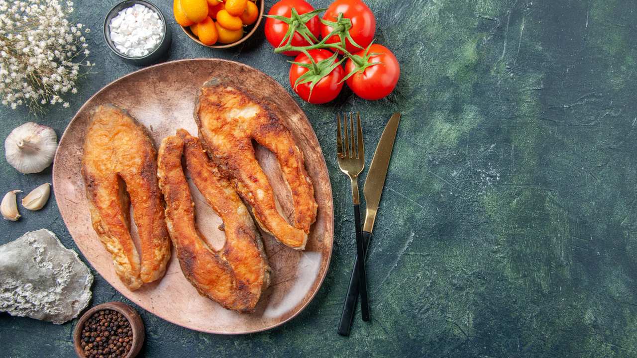 Peixe frito em prato, acompanhado de tomate, alho e outros ingredientes.