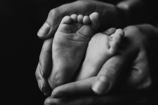 Pés de bebê em mãos adultas em preto e branco, simbolizando cuidado e proteção.