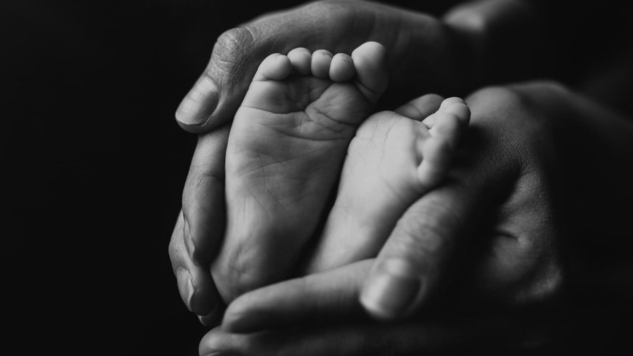 Pés de bebê em mãos adultas em preto e branco, simbolizando cuidado e proteção.