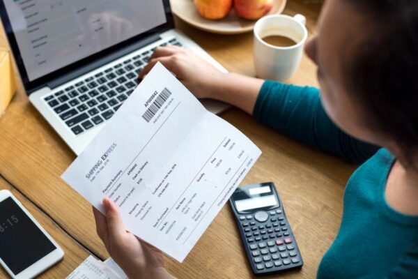 Pessoa analisa conta em computador, com calculadora e celular próximos.