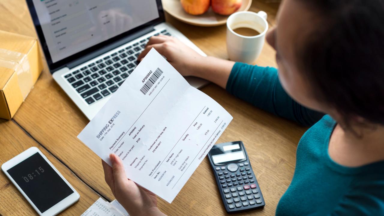 Pessoa analisa conta em computador, com calculadora e celular próximos.