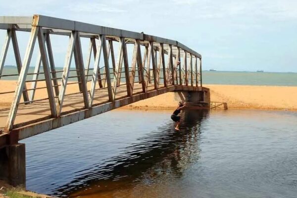 Pessoa pulando de ponte em praia de areia clara.
