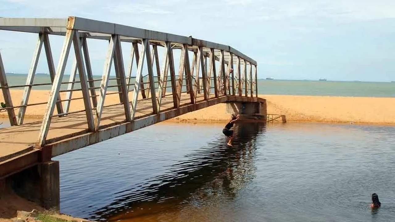 Pessoa pulando de ponte em praia de areia clara.