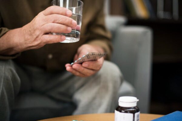 Pessoa segurando um copo d'água e comprimidos, possivelmente tomando medicação para problemas cardíacos.