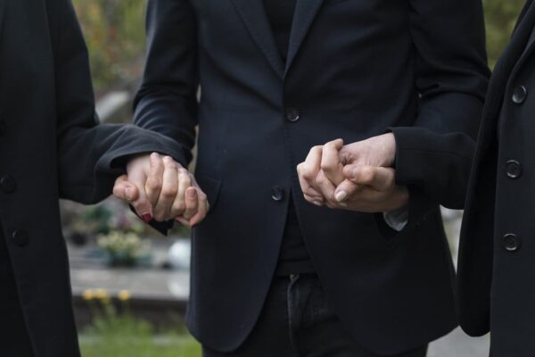 Pessoas de luto segurando as mãos em apoio, em um funeral.
