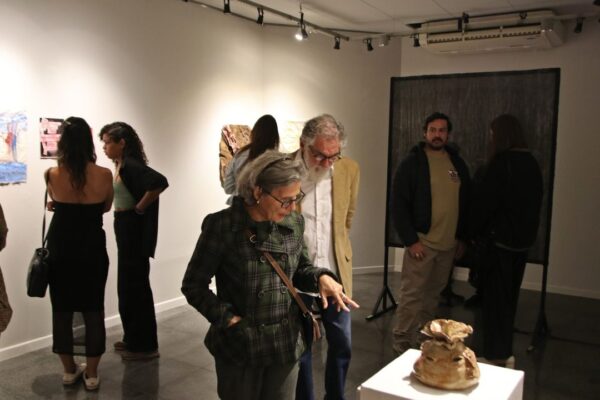 Pessoas em exposição de arte, com obras nas paredes e uma escultura em destaque.
