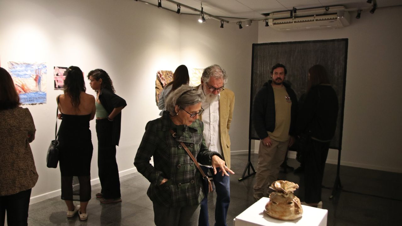 Pessoas em exposição de arte, com obras nas paredes e uma escultura em destaque.