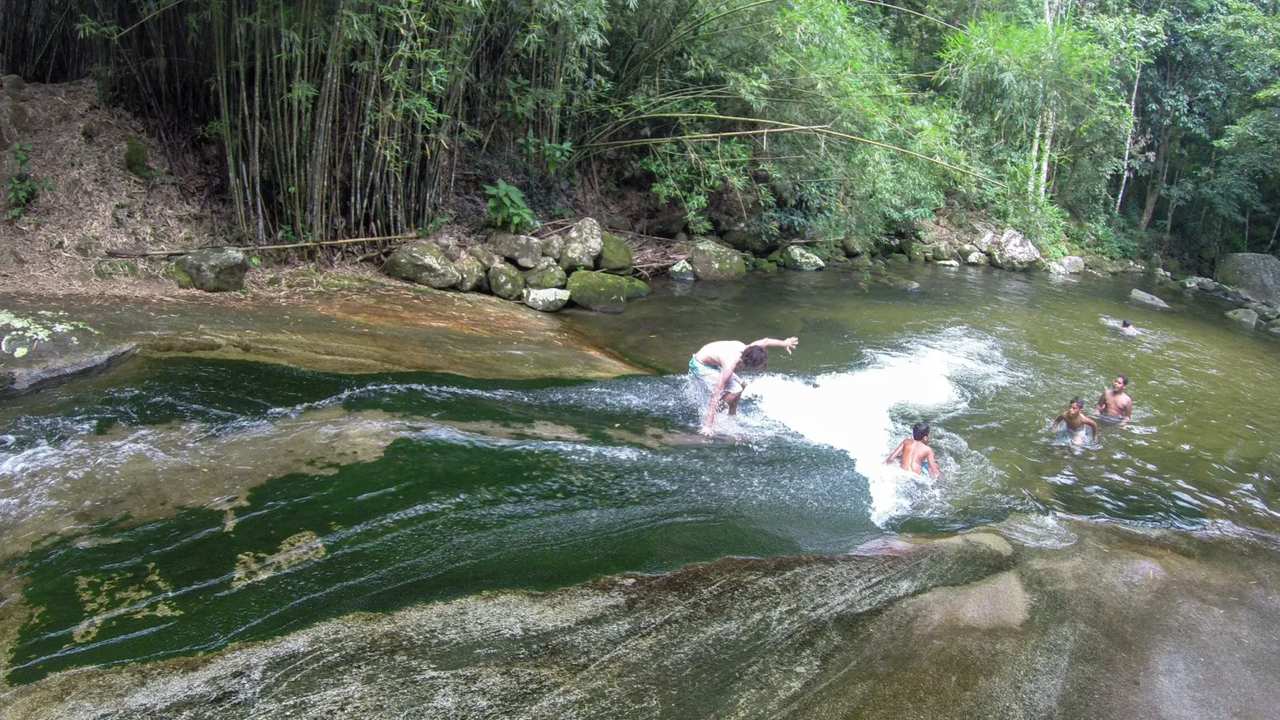 Pessoas se divertindo na Cachoeira do Escorrega, um tobogã natural em meio à natureza exuberante.
