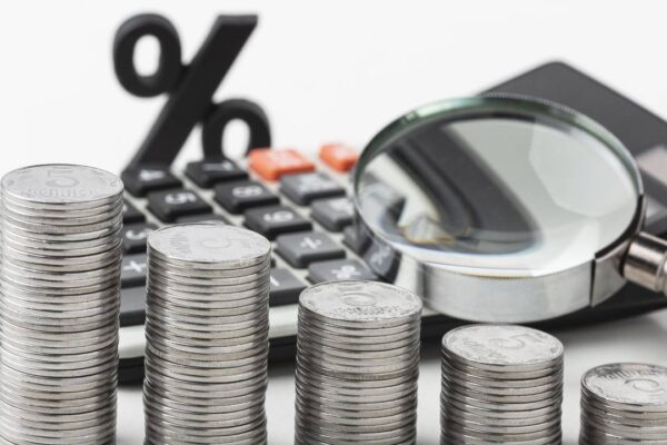 Pilhas de moedas com calculadora e lupa, simbolizando impostos sobre construção.