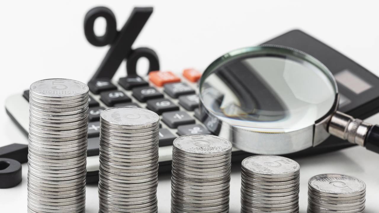 Pilhas de moedas com calculadora e lupa, simbolizando impostos sobre construção.