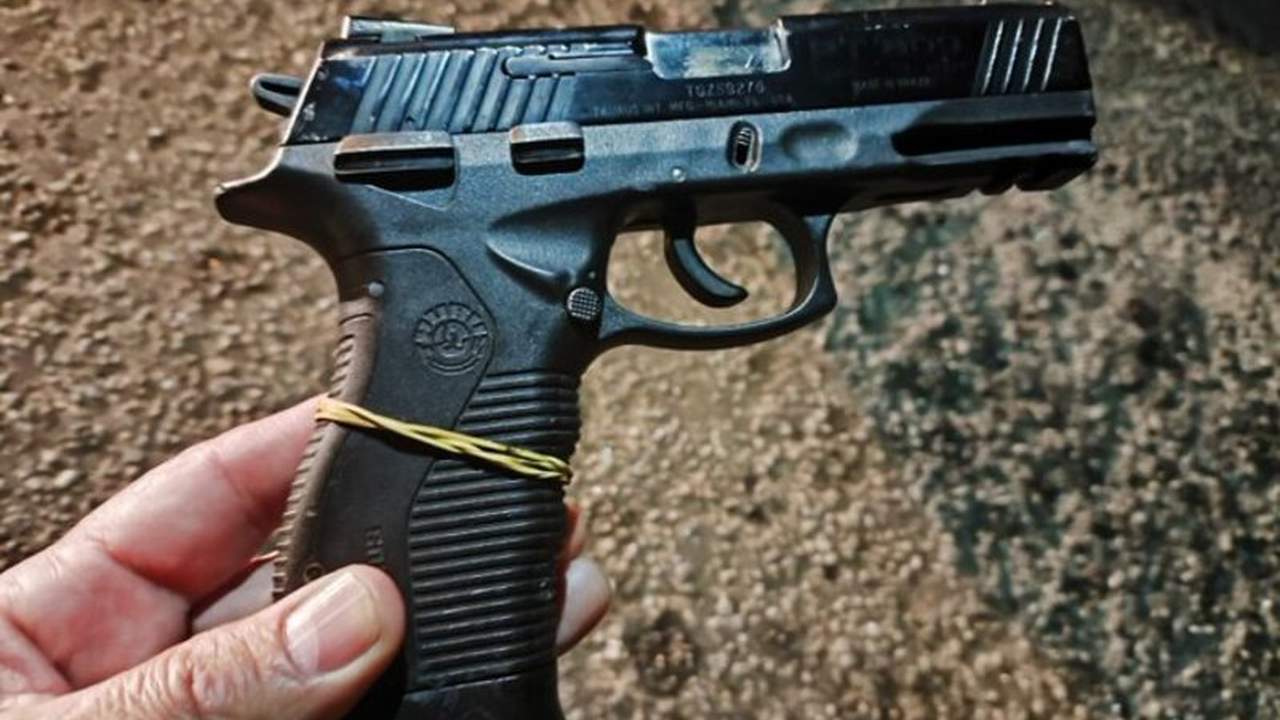 Pistola preta, usada em crime, vista de cima, foco na arma e não na pessoa.