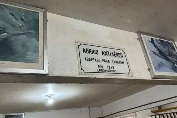 Placa 'Abrigo Antiaéreo' adaptado para garagem no Rio de Janeiro, com fotos de aviões emolduradas.