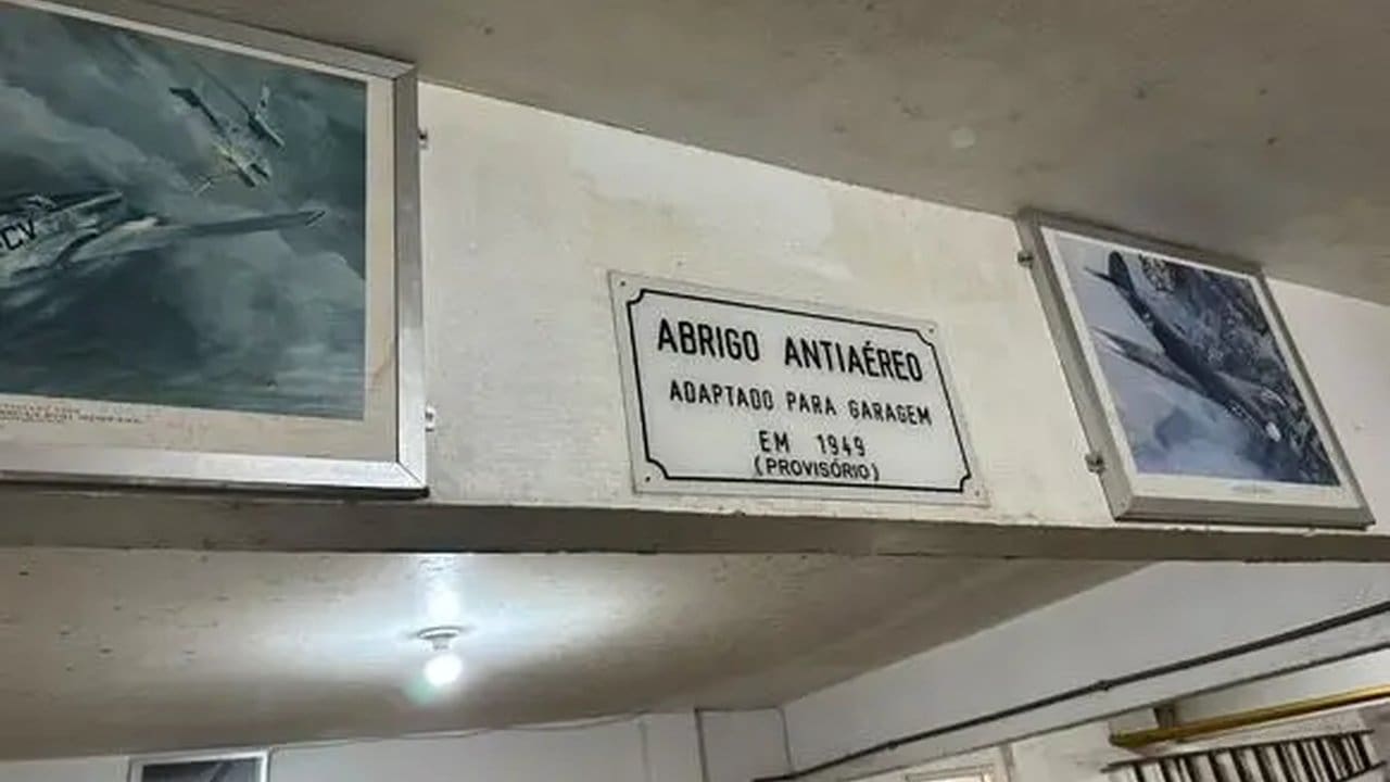 Placa 'Abrigo Antiaéreo' adaptado para garagem no Rio de Janeiro, com fotos de aviões emolduradas.