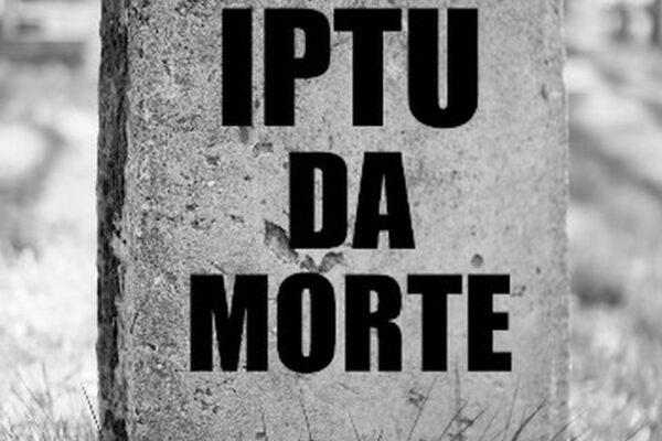 Placa de pedra com a inscrição IPTU da Morte em letras pretas, em um cemitério.