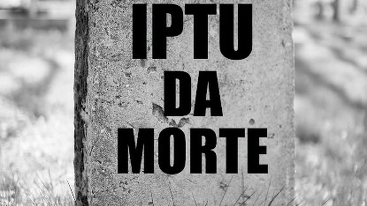 Placa de pedra com a inscrição IPTU da Morte em letras pretas, em um cemitério.