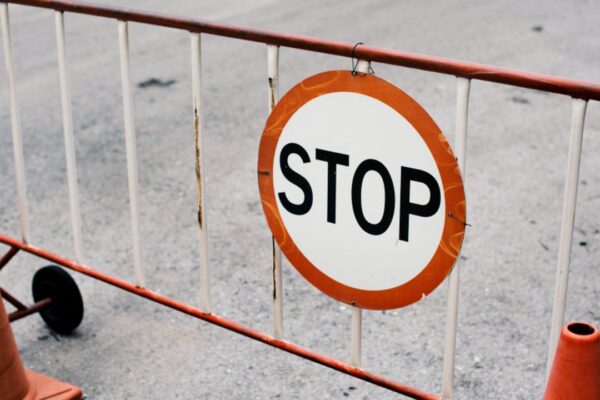 Placa de 'Stop' em barreira de obras, com cones de sinalização.