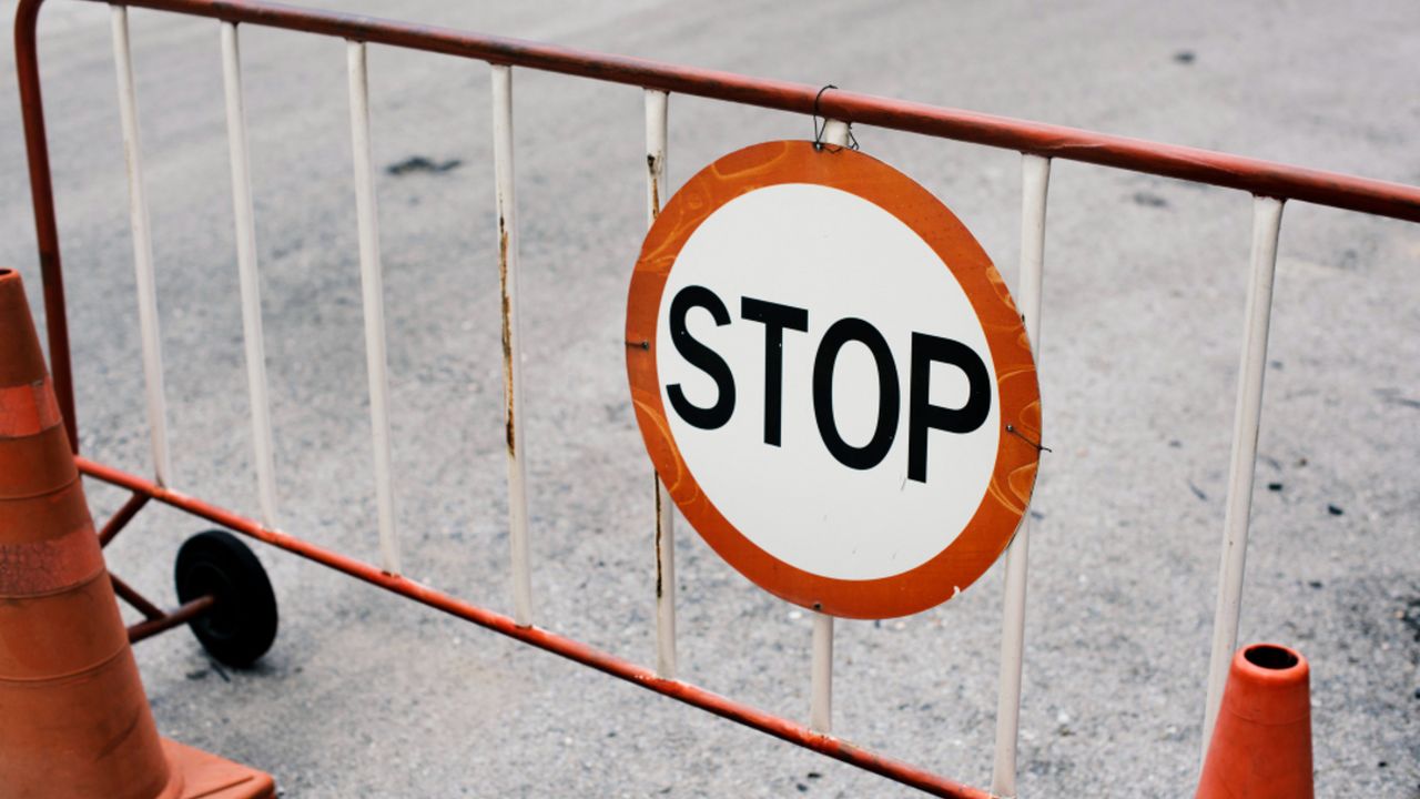 Placa de 'Stop' em barreira de obras, com cones de sinalização.
