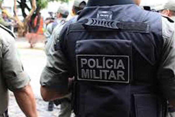 Policial militar com colete tático com a inscrição 'POLÍCIA MILITAR' nas costas.