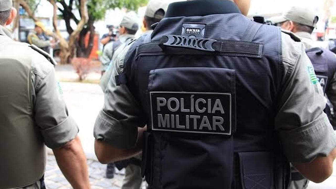 Policial militar com colete tático e a inscrição 'Polícia Militar'.
