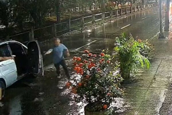 Policial militar sendo baleado próximo a carro em rua alagada.