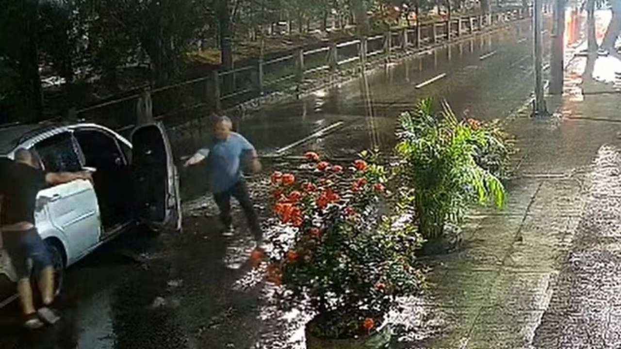 Policial militar sendo baleado próximo a carro em rua alagada.