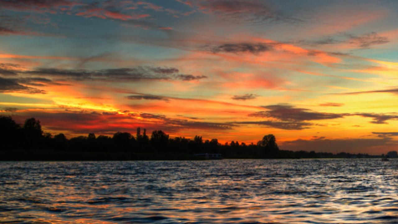 Por do sol sobre a água com silhueta de árvores na margem.