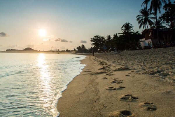 Praia ao pôr do sol com pegadas na areia, sugerindo Horário de Verão.