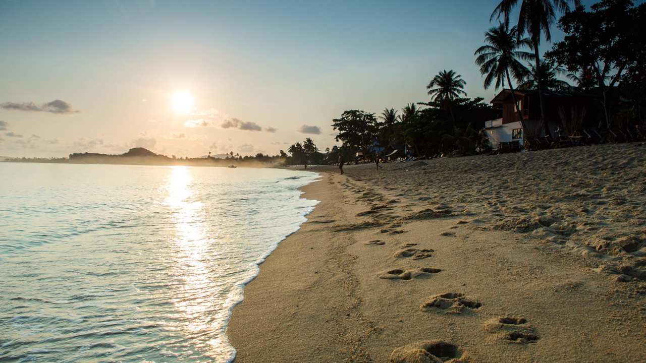Praia ao pôr do sol com pegadas na areia, sugerindo Horário de Verão.