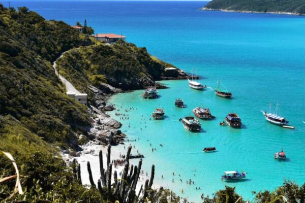 Praia de Búzios com barcos e mar azul turquesa, com vegetação exuberante.
