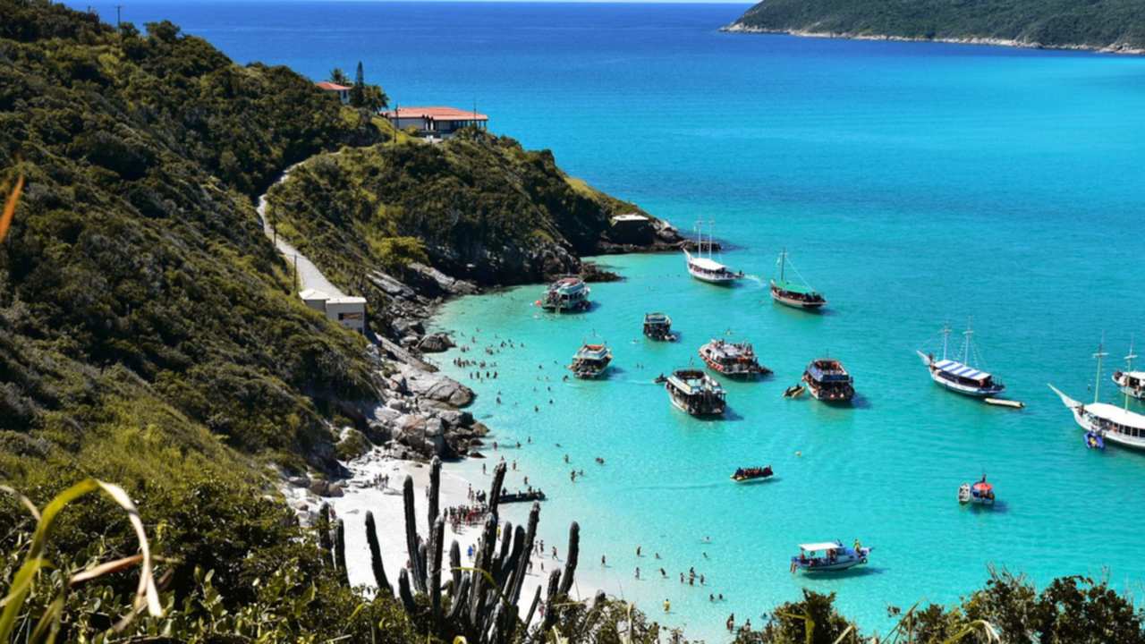 Praia de Búzios com barcos e mar azul turquesa, com vegetação exuberante.