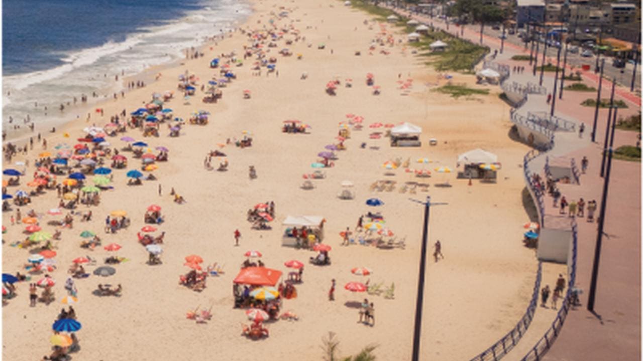 Praia de Maricá com guarda-sóis coloridos e pessoas aproveitando o dia ensolarado.