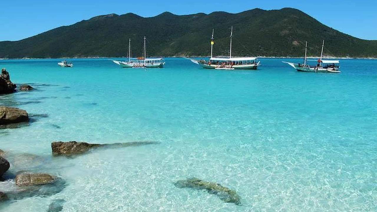 Praia do Farol em Arraial do Cabo, com águas cristalinas e barcos.