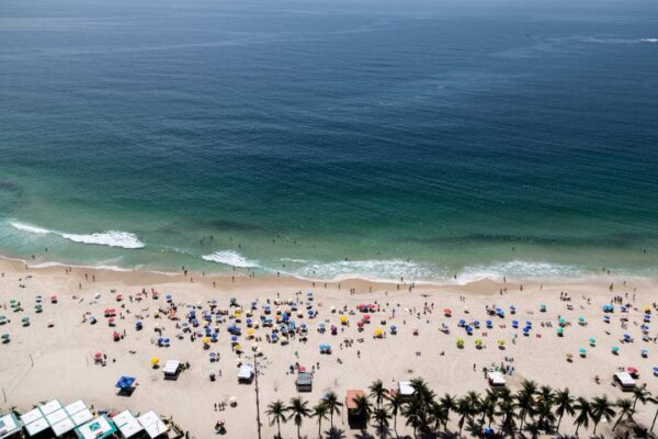 Praia ensolarada com guarda-sóis e banhistas, possivelmente no Brasil.