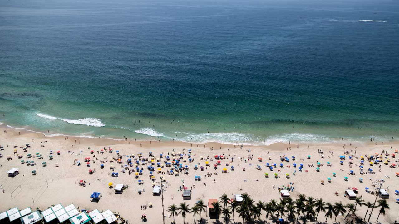 Praia ensolarada com guarda-sóis e banhistas, possivelmente no Brasil.