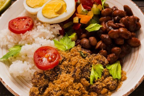 Prato de comida brasileira com arroz, feijão, farofa, tomate e ovo cozido.