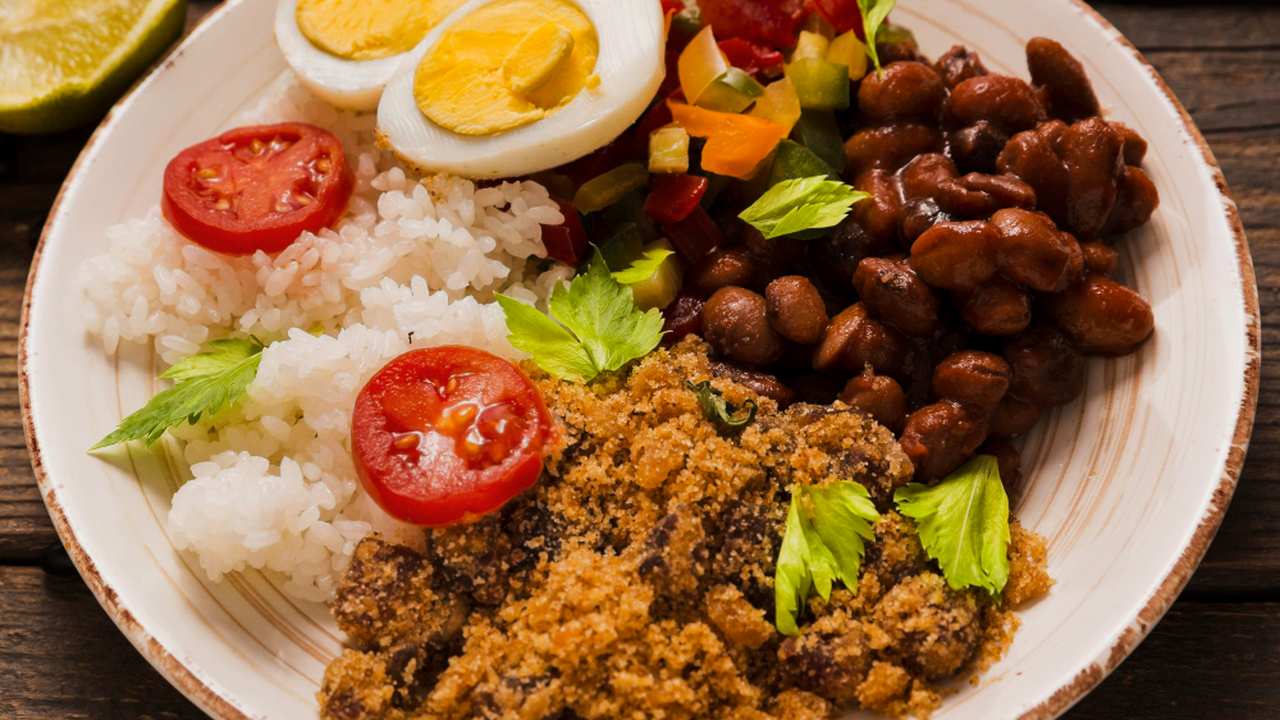 Prato de comida brasileira com arroz, feijão, farofa, tomate e ovo cozido.