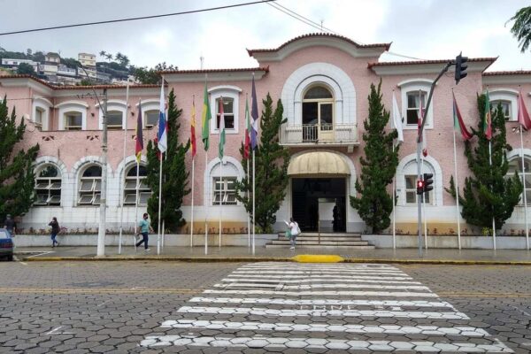 Prédio da Prefeitura de Nova Friburgo com bandeiras e pessoas na rua.