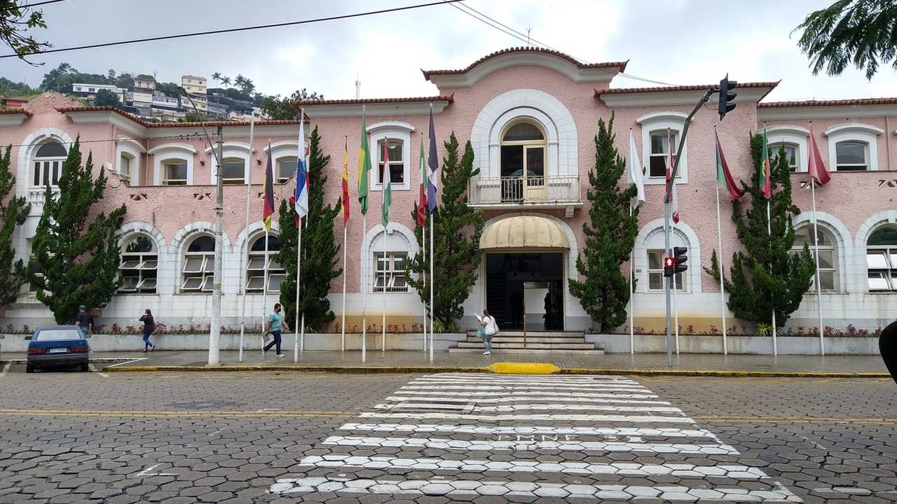Prédio da Prefeitura de Nova Friburgo com bandeiras e pessoas na rua.