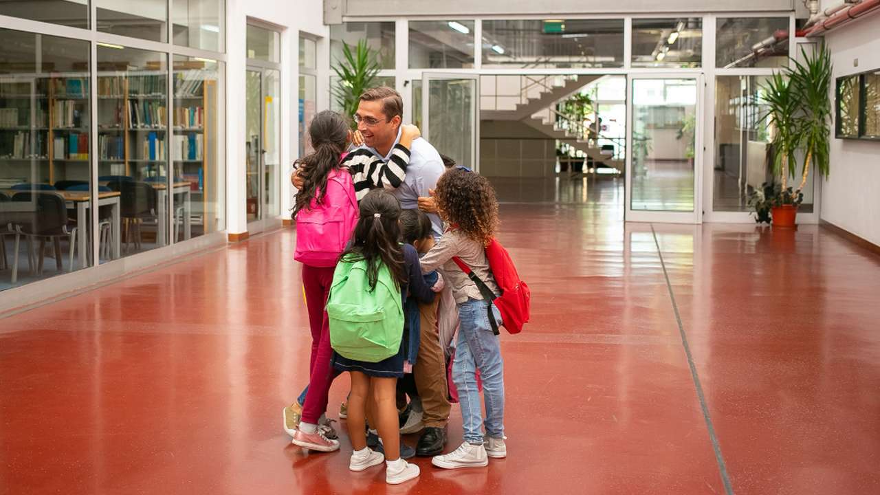 Professor abraçando alunos em escola.