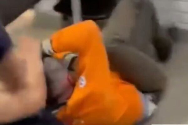 Professor sendo agredido por um homem em uniforme laranja.