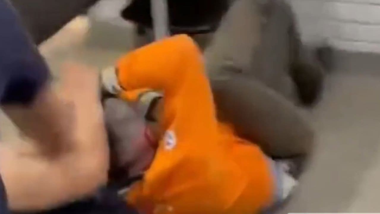 Professor sendo agredido por um homem em uniforme laranja.