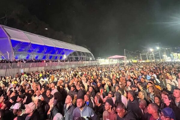 Público reunido em frente a um palco em um evento, à noite.