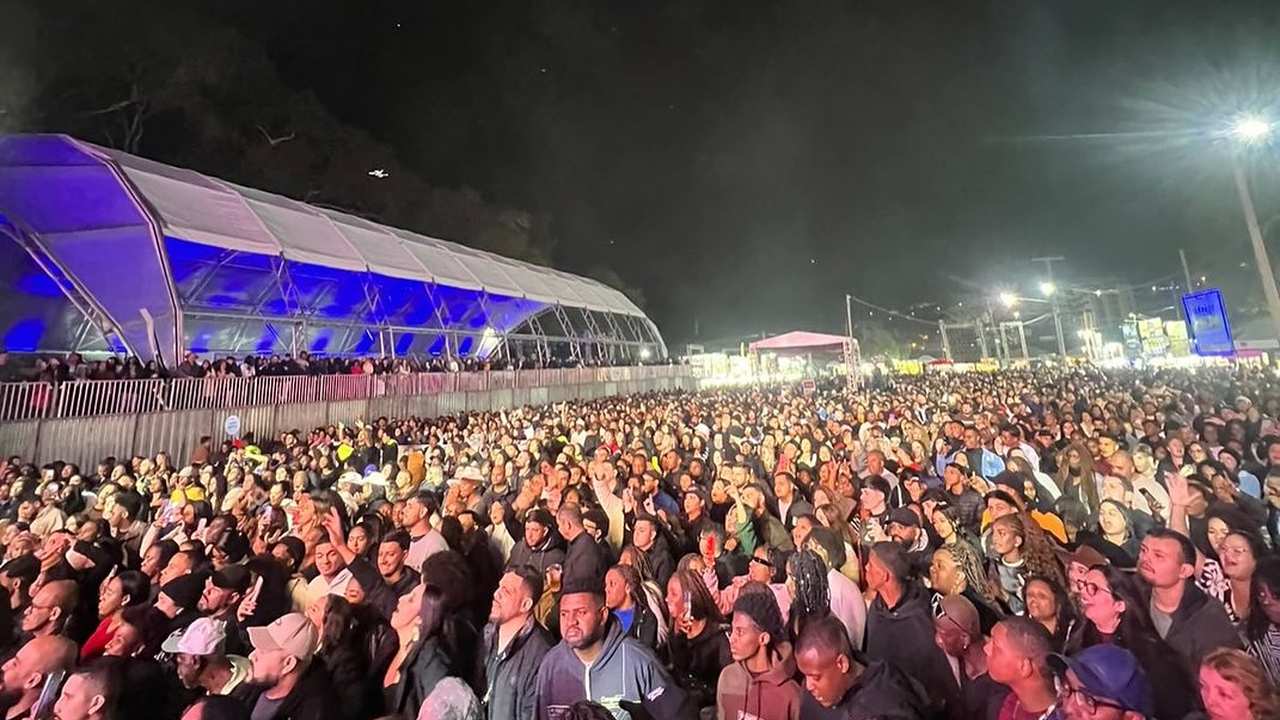 Público reunido em frente a um palco em um evento, à noite.