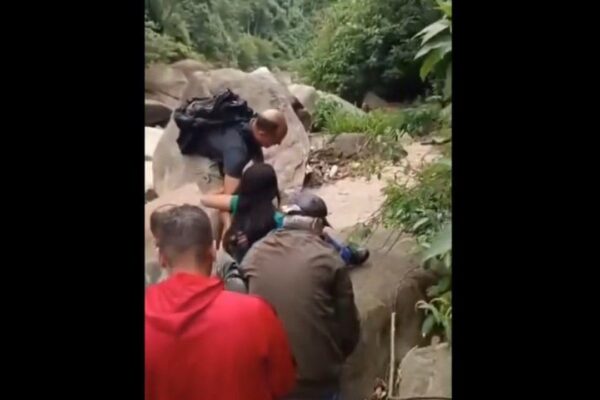 Resgate de mulher em área de mata, com pessoas ajudando.