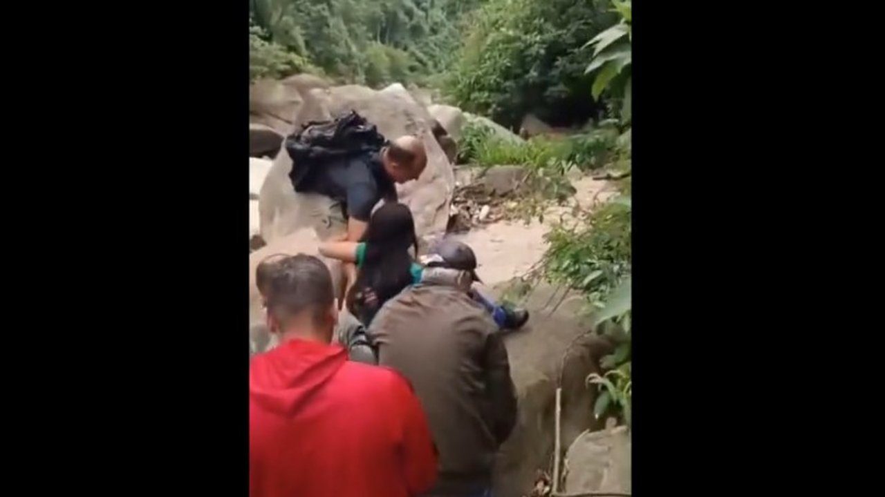 Resgate de mulher em área de mata, com pessoas ajudando.