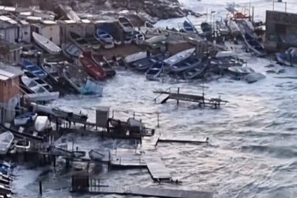 Ressaca marítima atinge a costa, com ondas violentas e barcos danificados.