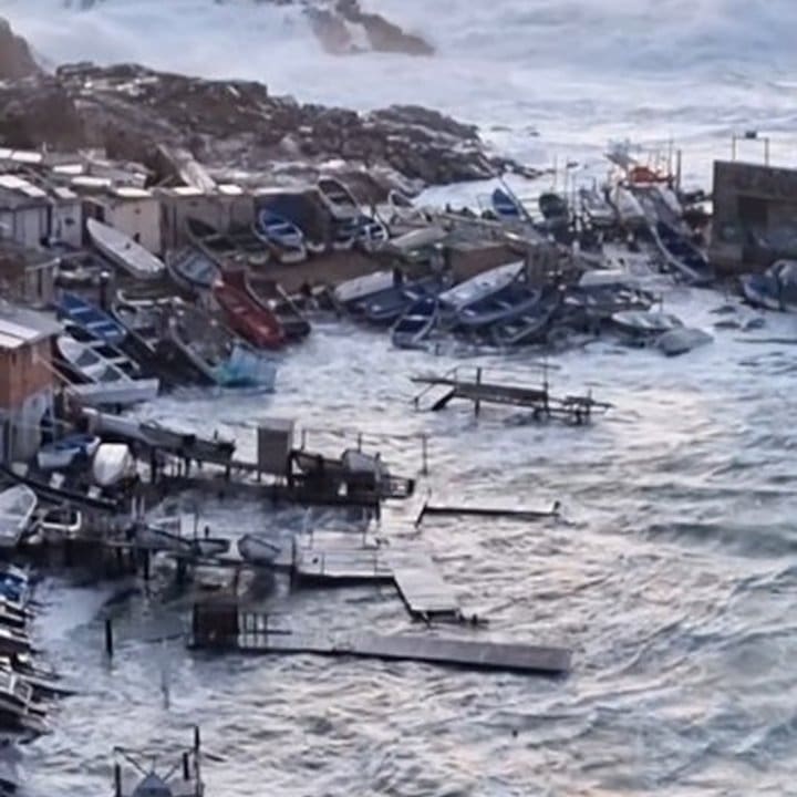 Ressaca marítima atinge a costa, com ondas violentas e barcos danificados.