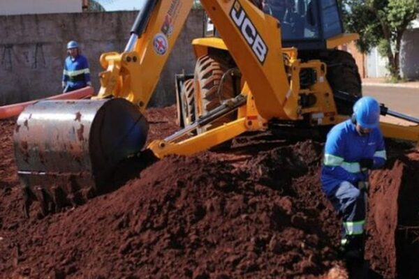 Retroescavadeira amarela em obras, com operários trabalhando em Nova Friburgo.
