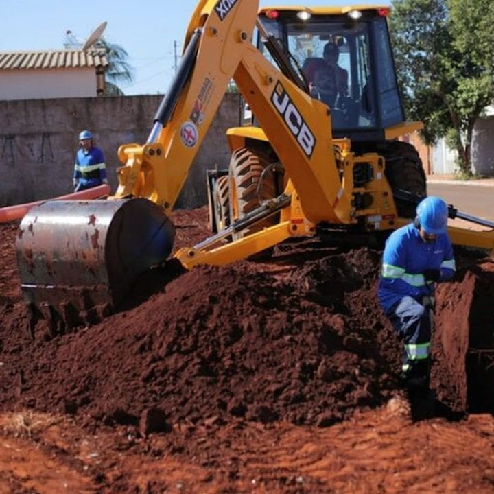 Retroescavadeira amarela em obras, com operários trabalhando em Nova Friburgo.